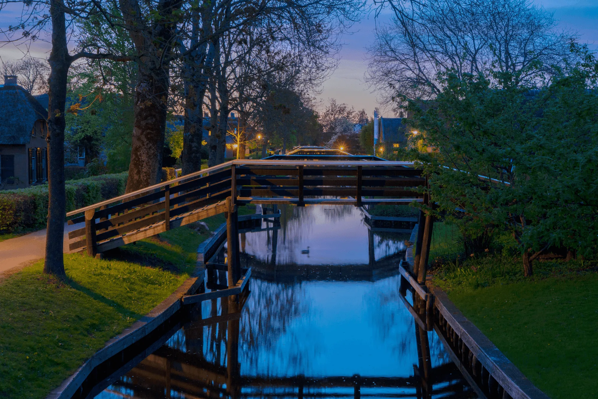 Houten brug over rustige gracht in Giethoorn bij schemering